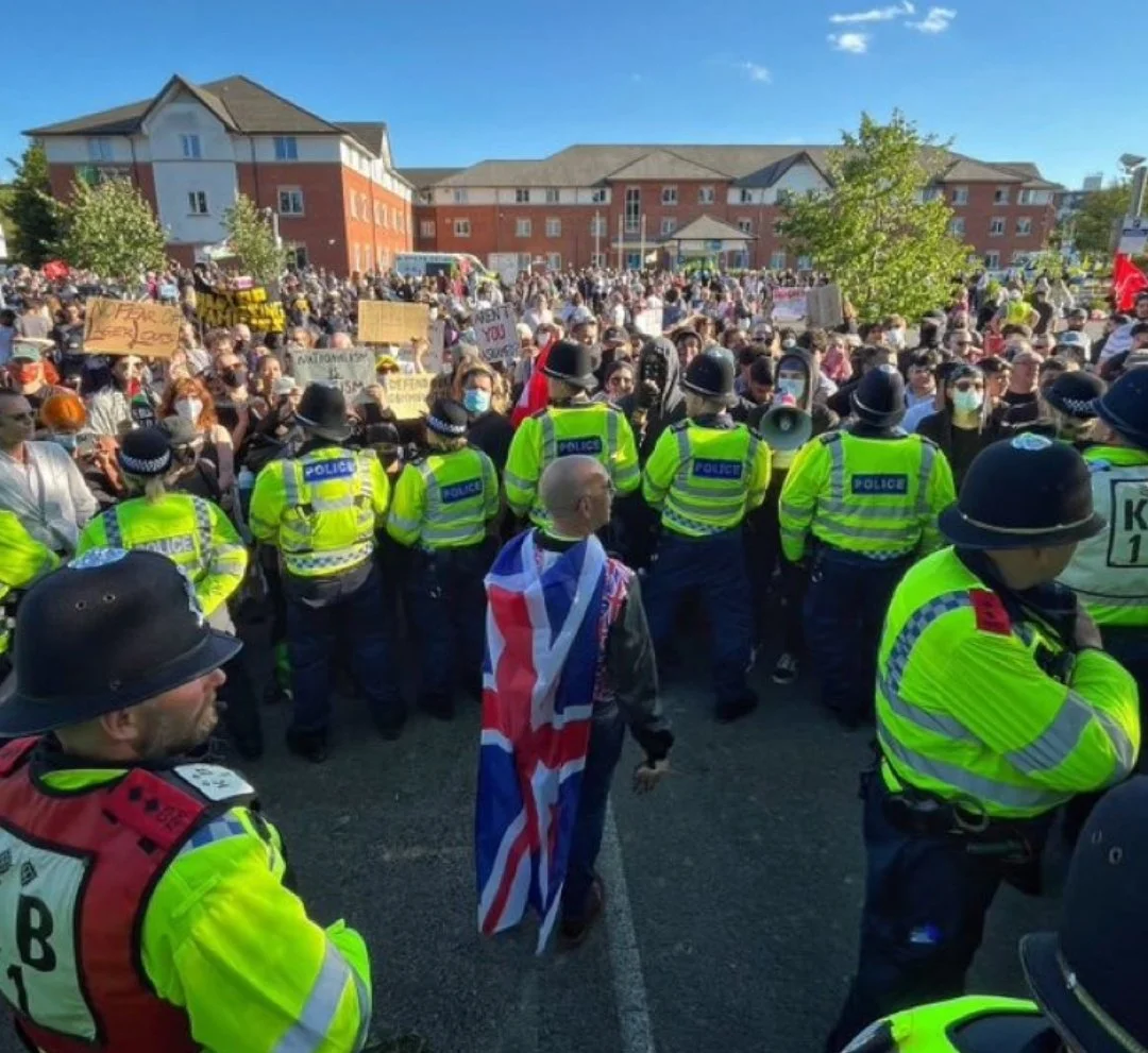 A single racist is separated from a large crowd of anti-racist protesters by a line of police officers